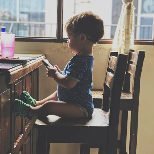 Un bébé assis seul sur une chaise avec un smartphone dans les mains