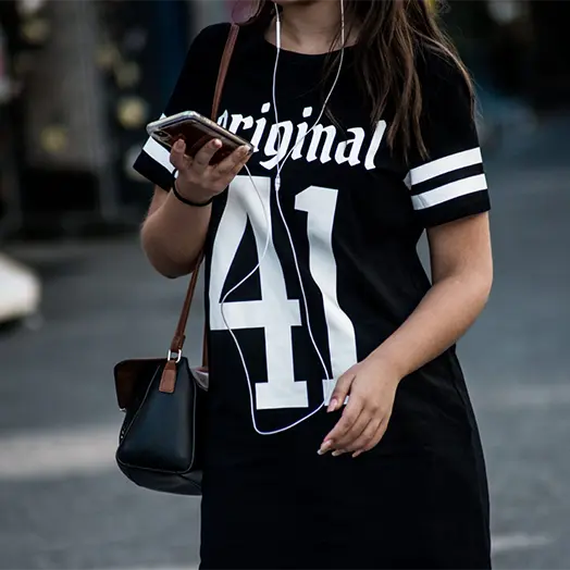 Une jeune fille dans la rue le regard porté sur son smartphone avec des écouteurs